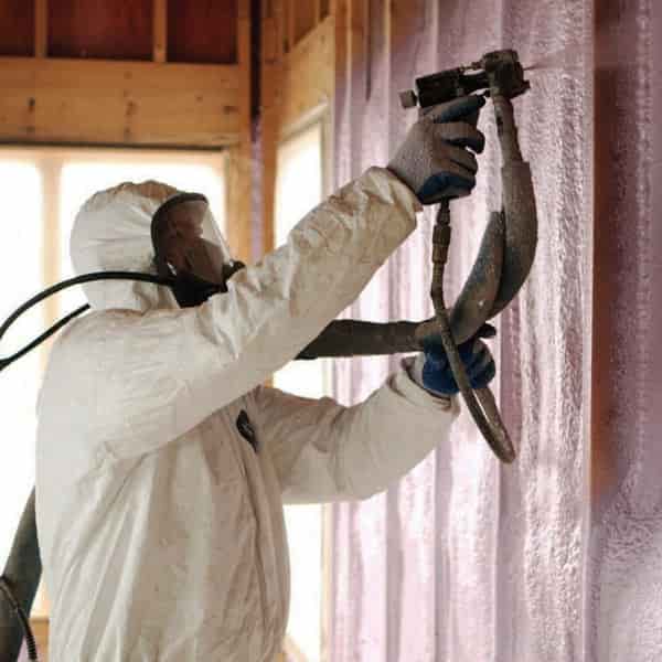 Spray foam insulation is being applied to the interior wall by the fully suited and masked worker.